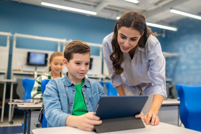 Profesoară și elev, lucrând cu o tabletă la clasă